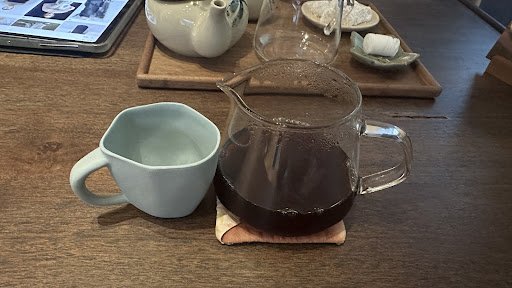 A close-up of a table setting in what appears to be an indoor cafe or restaurant with various items including a ceramic teapot, tea cups, and a glass