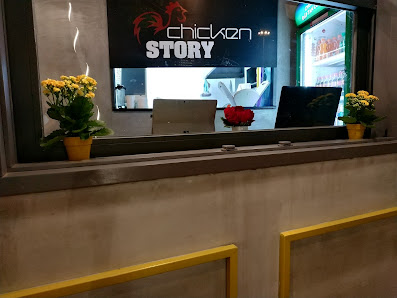 The image shows an interior view of a restaurant named 'Chicken Story'. The counter has yellow trim and there are potted plants on either side, with t