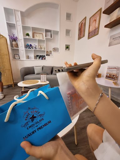 A person is holding a blue shopping bag from 'Palm Place Chocolate Luxury Premium' and appears to be in the process of unboxing or showing off an item