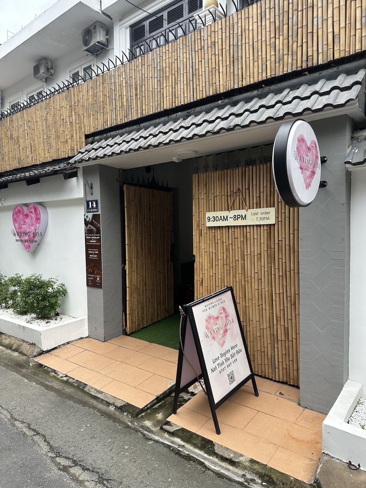 Exterior view of Waxing Hoa, a beauty salon located in Thao Dien, Saigon. Features include a bamboo facade on the building, a circular sign with a pin