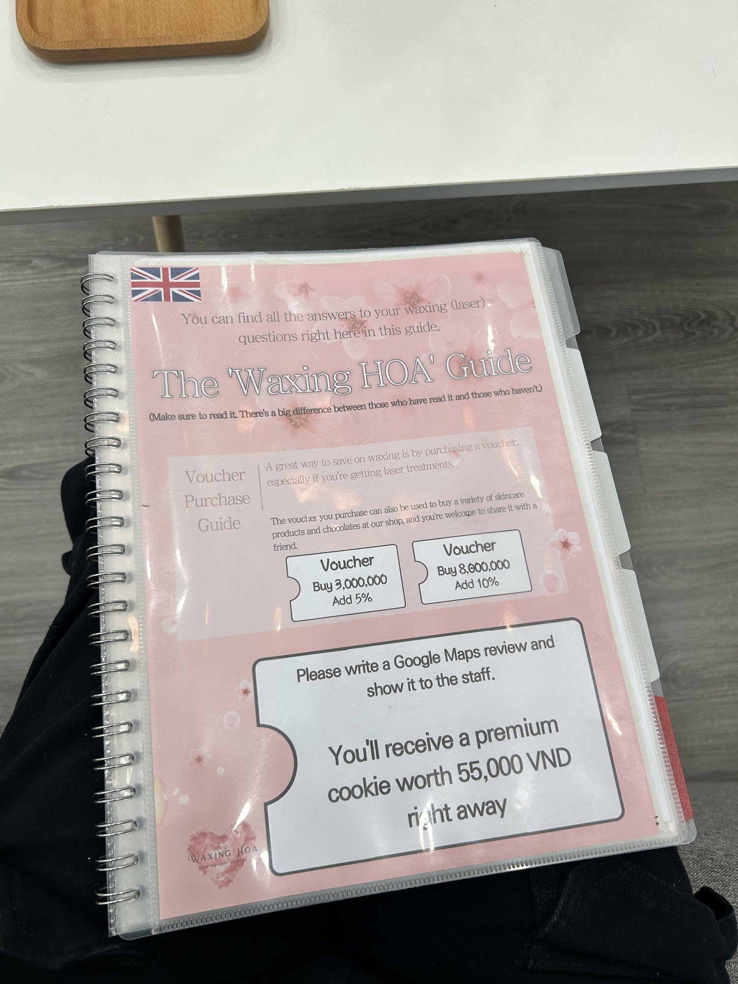 The image shows a spiral-bound promotional guide titled 'The 'Waxing HOA' Guide' with a pink background and UK flag. It contains information about wax