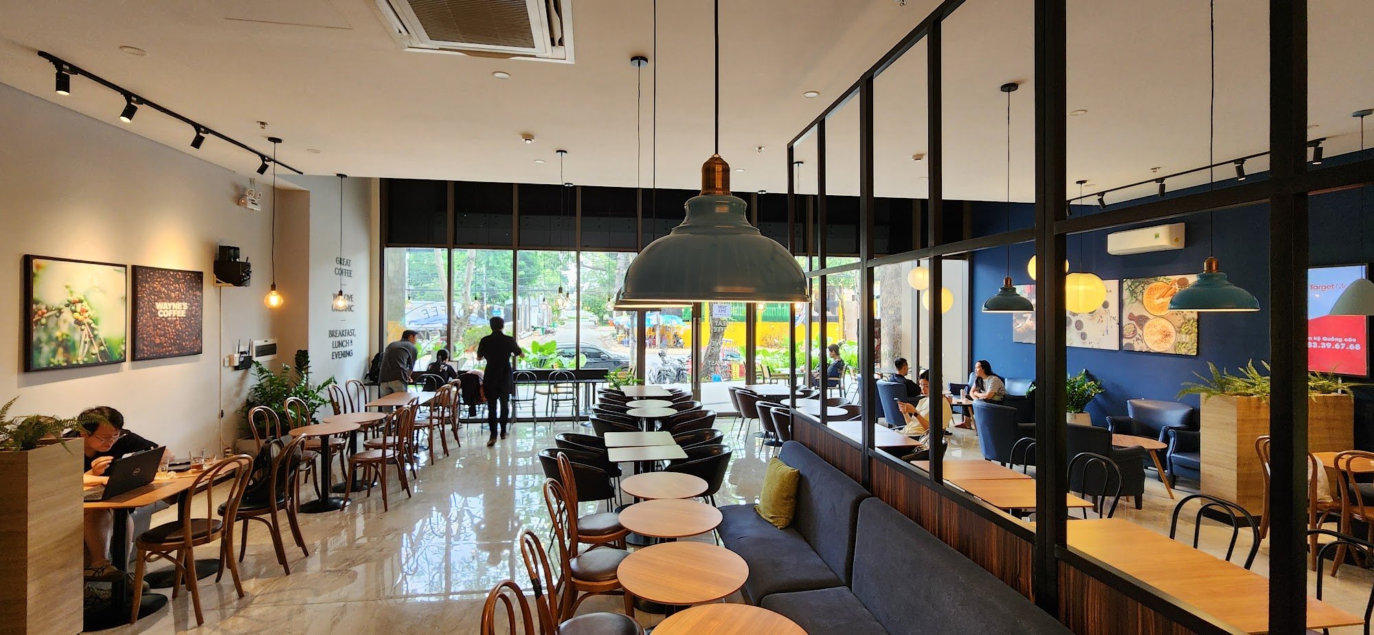 The image shows an interior view of a modern coffee shop or restaurant in Thao Dien, Saigon. The space is well-lit with natural light coming through l