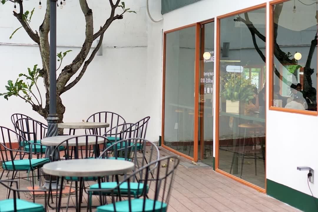 The image shows an outdoor seating area of a venue in Thao Dien, Saigon with several round tables and chairs arranged on the patio. The furniture has 