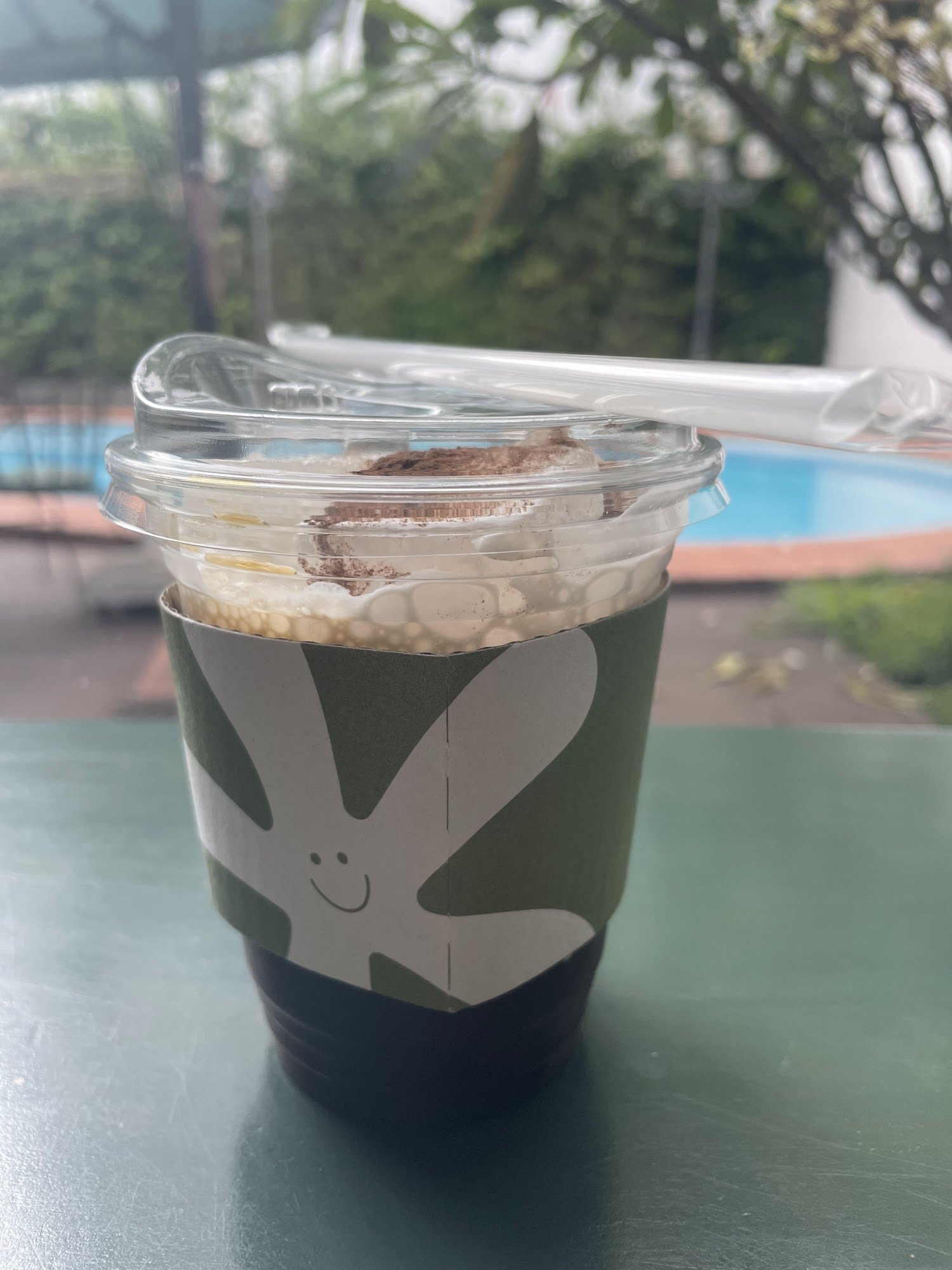 A close-up of a beverage in a takeaway cup featuring a cartoon character on the side and topped with what appears to be whipped cream or foam, possibl