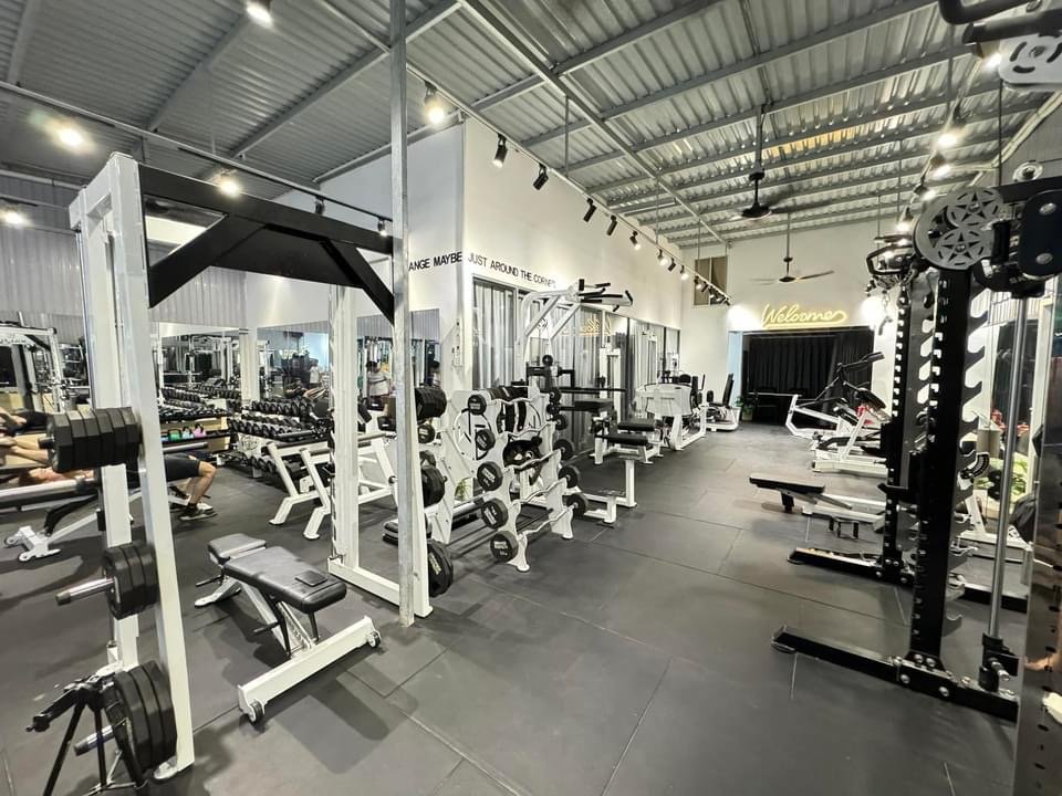 The image shows a well-equipped gym interior featuring various weightlifting machines and free weights on racks.