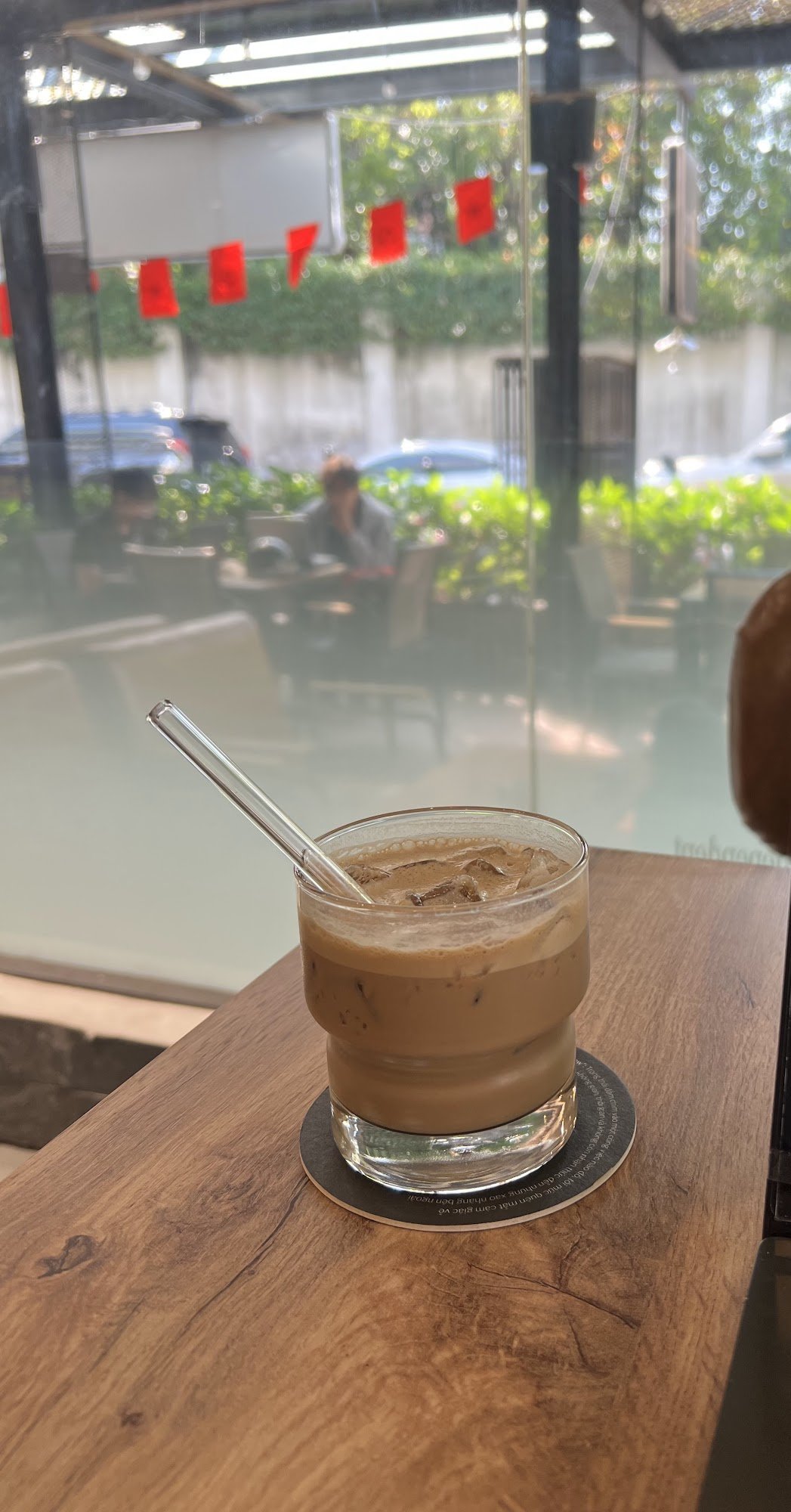 A glass of cold coffee beverage on a wooden table at an outdoor cafe setting.