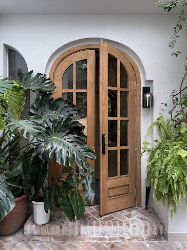 The image depicts the exterior entrance of a venue in Thao Dien, Saigon. It features a wooden arched double door with glass panels, set within a white