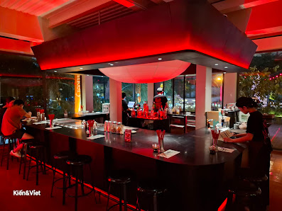 The image depicts the interior of a modern bar or restaurant in Thao Dien, Saigon. It features a long black bar counter with high stools, illuminated