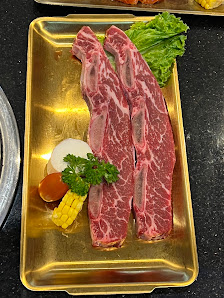 A close-up of a plate containing two pieces of raw beef steak garnished with corn kernels and green lettuce on the side, served on a golden tray.