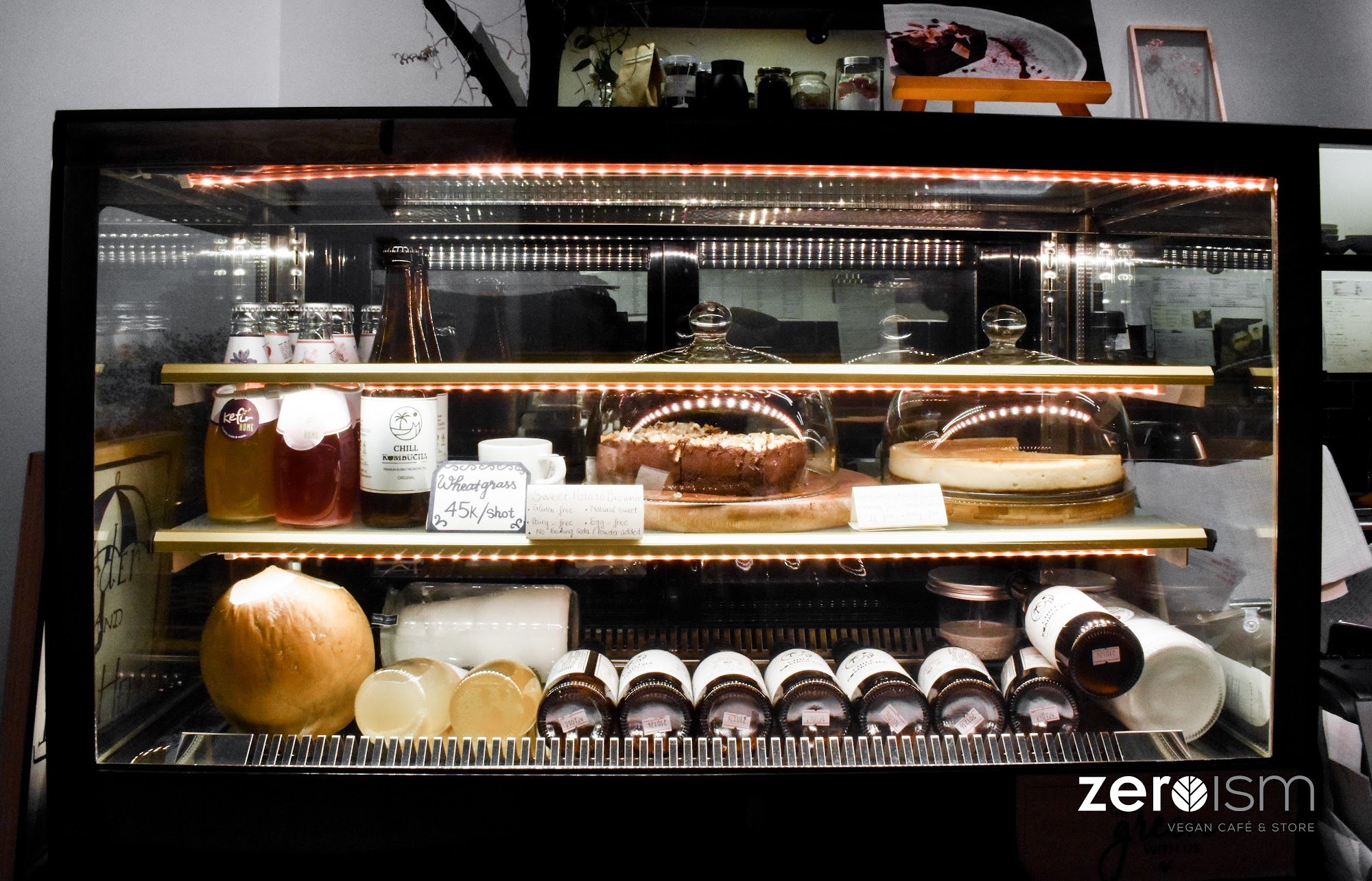 The image shows a display case in an establishment named 'zeroism', which appears to be a vegan cafe and store, as indicated by the signage at the bot
