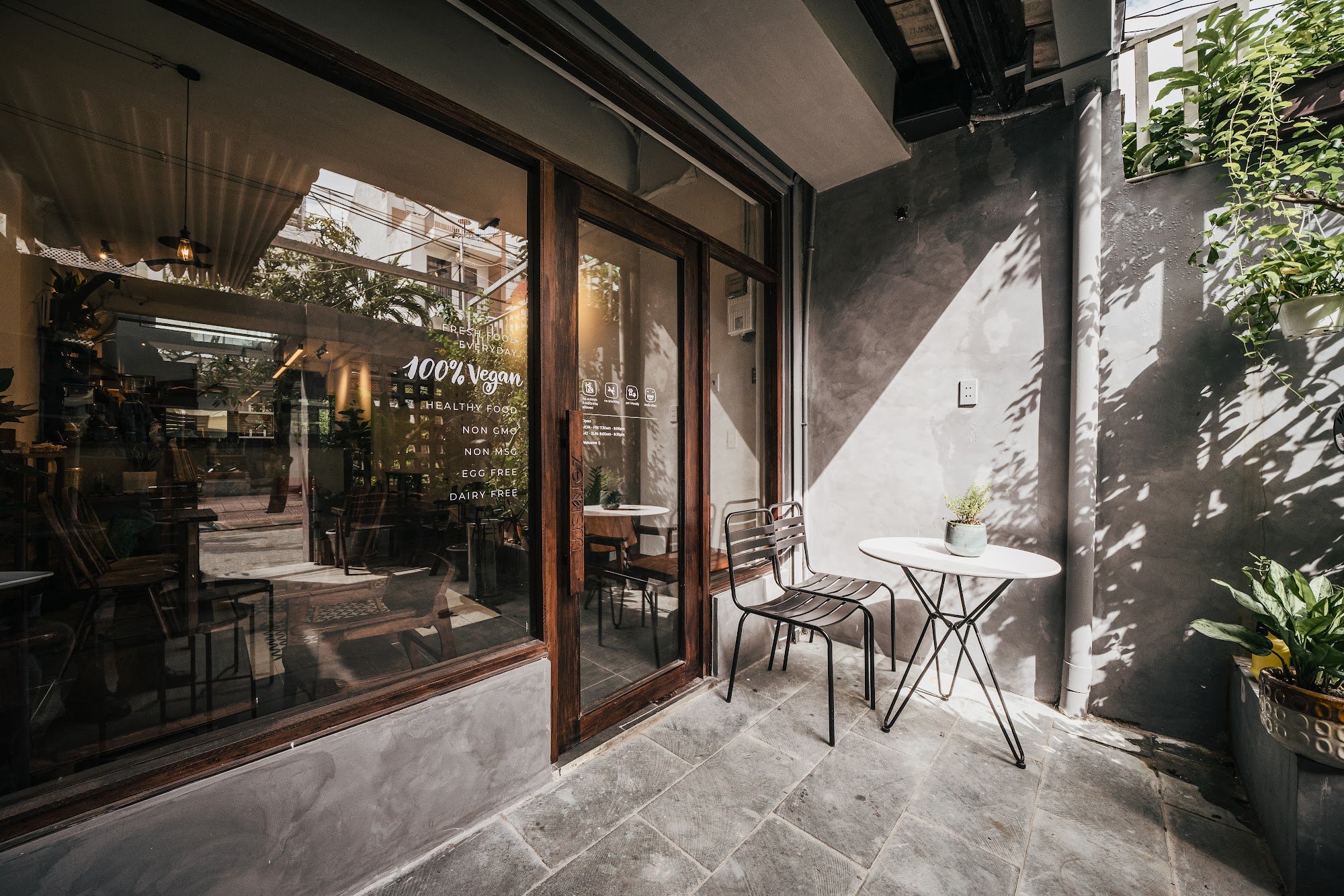 The image shows an exterior view of a modern cafe or restaurant located in Thao Dien, Saigon. The establishment has large glass windows with text indi