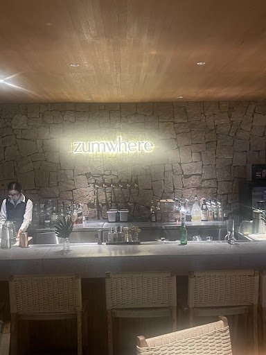 The image depicts the interior of a bar named "zumWhere" located in Thao Dien, Saigon. It features a stone wall backdrop with the illuminated "zumWher